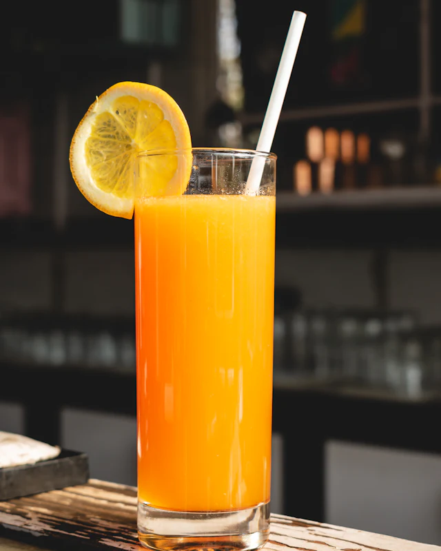 Glass of orange juice with a lemon slice and straw